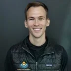 Headshot of Miles King, smiling, wearing a black vest with Bristol Bay Foundation and Patagonia logos against a dark gray background.