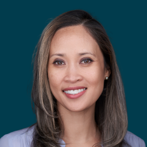 Headshot of Cherry Cayabyab, smiling, with shoulder-length dark hair and gray highlights, wearing pearl earrings and a light blue top against a dark ocean-blue background.