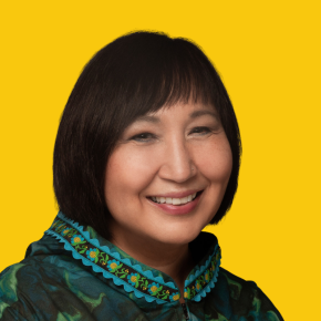 Headshot of Deborah Vo, smiling, with short black hair, wearing a teal patterned jacket with embroidered trim against a dandelion-yellow background.