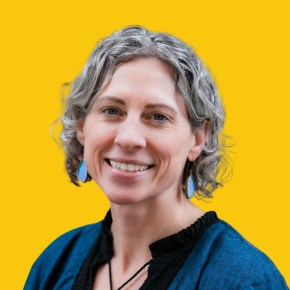 Headshot of Erin Switalski, smiling, with short curly gray hair, wearing blue drop earrings and a teal jacket over a black top against a dandelion-yellow background.