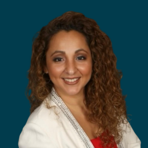 Headshot of Esther Richmond, smiling, with long curly light brown hair, wearing a white blazer over a red top against a dark ocean-blue background.