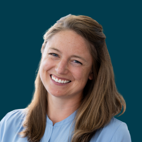 Headshot of Heather Flaherty, smiling, with long light brown hair, wearing a light blue blouse against a dark ocean-blue background.