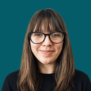Headshot of Jackie Doherty, smiling slightly, with long brown hair and bangs, wearing black glasses and a dark top against a dark ocean-blue background.