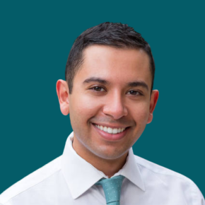 Headshot of Jaser Alsharhan, smiling, with short dark hair, wearing a white dress shirt and light teal tie against an ocean-blue background.