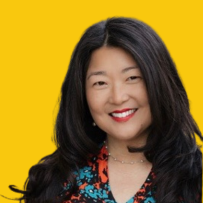 Headshot of Kara Carlisle, smiling, with long black hair, red lipstick, and a floral patterned blouse against a dandelion-yellow background.