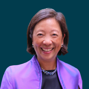Headshot of Melinda Tuan, smiling, with short brown hair, wearing a purple jacket over a black top and a beaded necklace against a dark ocean-blue background.