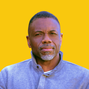 Headshot of Michael Brown, looking at the camera with a serious expression, wearing a gray pullover against a dandelion-yellow background.