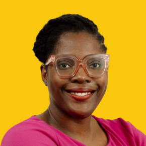 Headshot of Rachel Jackson, smiling, with pink-framed glasses and short natural hair, wearing a bright pink top against a dandelion-yellow background.