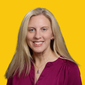Headshot of Rachel Konrad, smiling, with long blonde hair, wearing a magenta blouse and matching purple pendant necklace against a dandelion-yellow background.