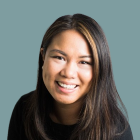 Headshot of Sheryl Saturnino Olivia, smiling, with long dark hair and subtle highlights, wearing a black top against a muted teal background.