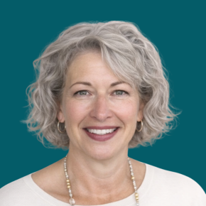 Headshot of Vicki Foege, smiling, with short curly silver hair, wearing hoop earrings, a beaded necklace and a light top against a dark ocean-blue background.