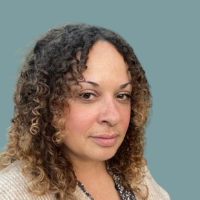 Headshot of Lacrecia Hill, looking at the camera with a slight smile, with shoulder-length curly hair and blonde highlights, wearing a cream cardigan against a muted teal background.