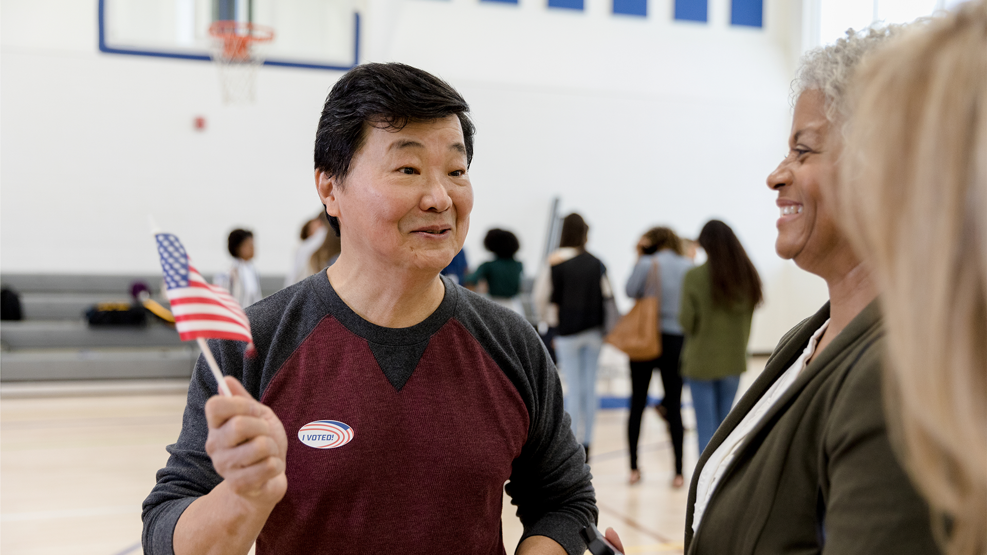 Man with an American flag talking to women at a voting center