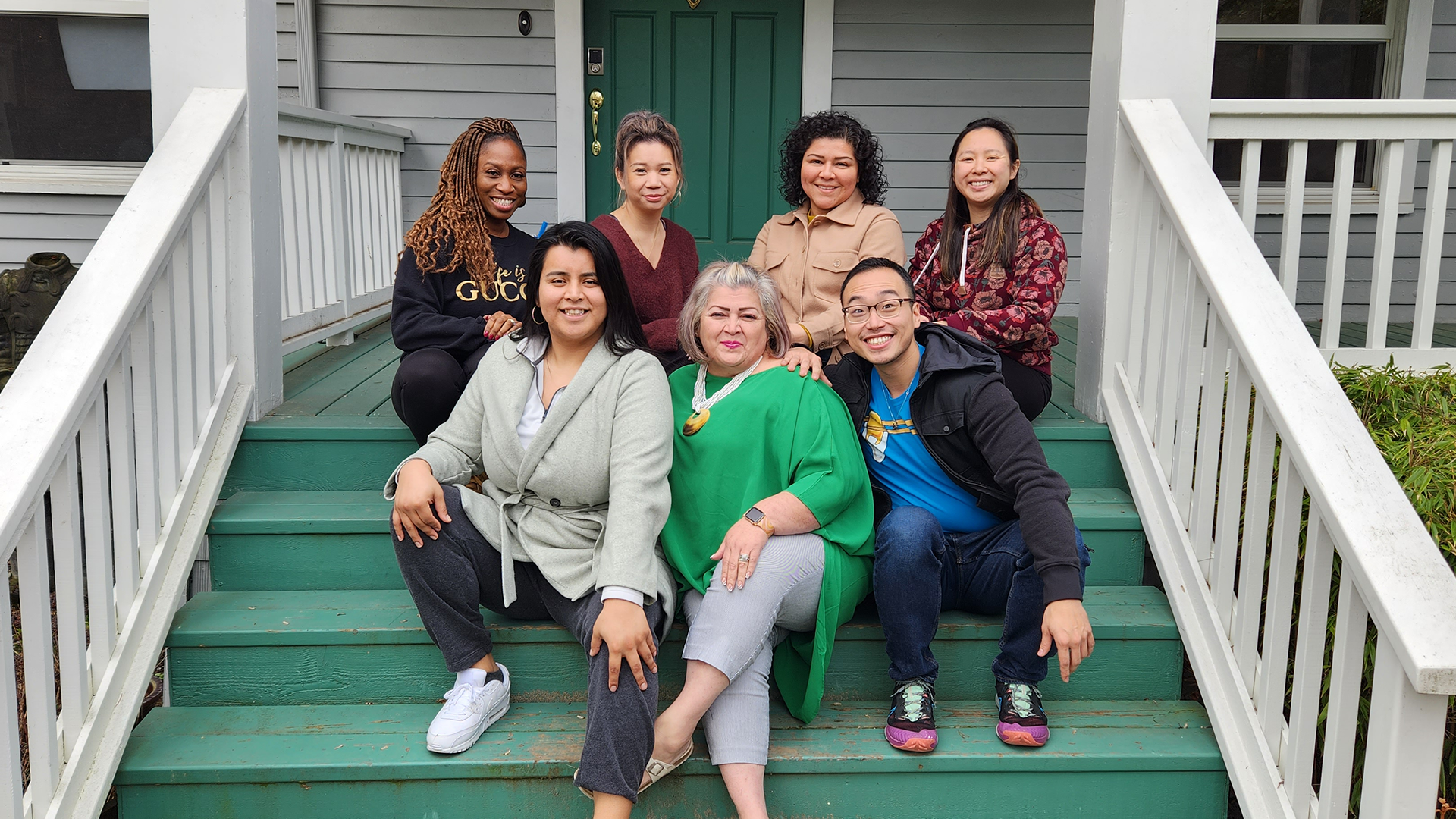 Cohort Four Momentum Fellows sitting outdoors on the green steps of a house in Seattle.
