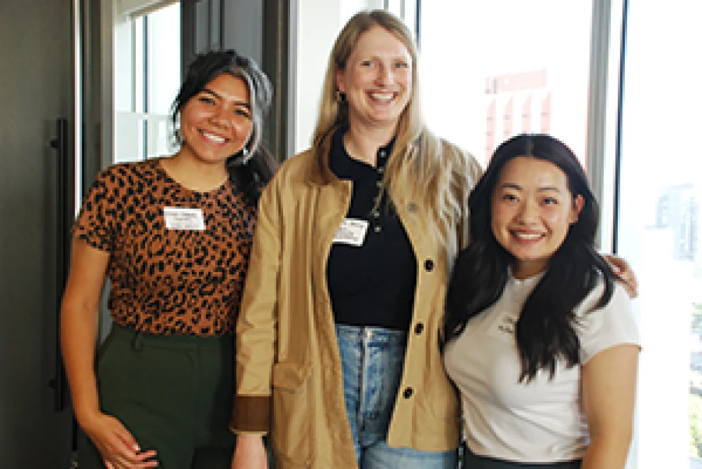Three attendees standing together at Philanthropy Northwest’s Regional Community Philanthropy Group fall 2025 convening in Seattle, wearing name tags and casual business attire, with large windows and city buildings visible in the background.