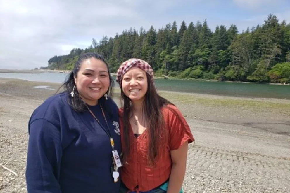 Two people standing together on a beach with trees in the background.