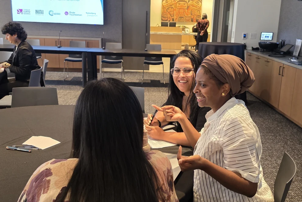 Photo of Mares Asfaha, Michaela Brown and another attendee talking around a table at a Seattle Membership Tour event, with a presentation screen and meeting room setup in the background.