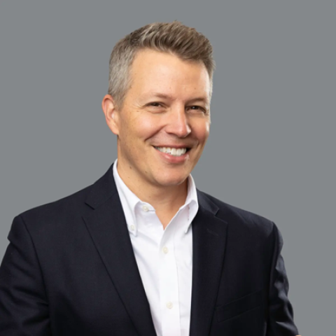 Headshot of Matt Morton smiling, wearing a dark blazer and white shirt against a plain gray background.