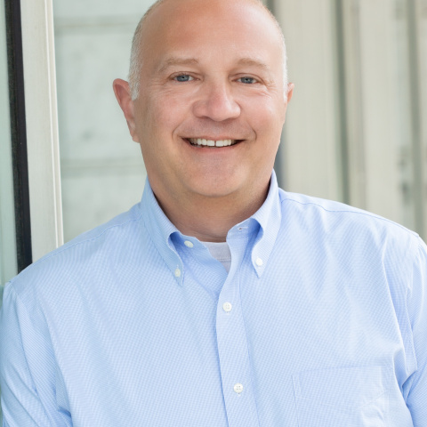 Chris Nanni headshot, wearing a blue shirt and smiling in front of a window