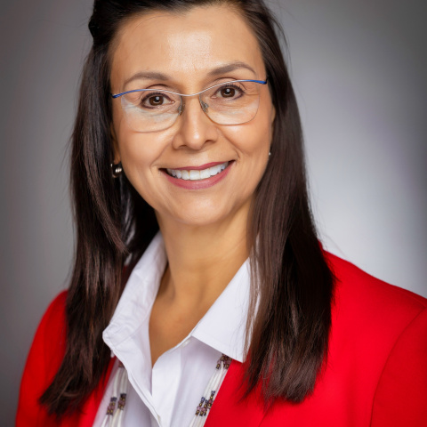 Monica Simeon headshot, Monica is smiling with brown hair and glasses, wearing a red blazer in front of a grey background