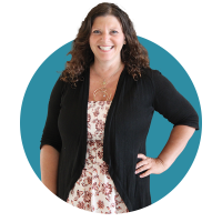 Headshot of Jeanine with curly brown hair standing with one hand on her hip. She wears a black cardigan over a floral dress and a circular pendant necklace, posed against a teal graphic background.  Select 70 more words to run Humanizer.