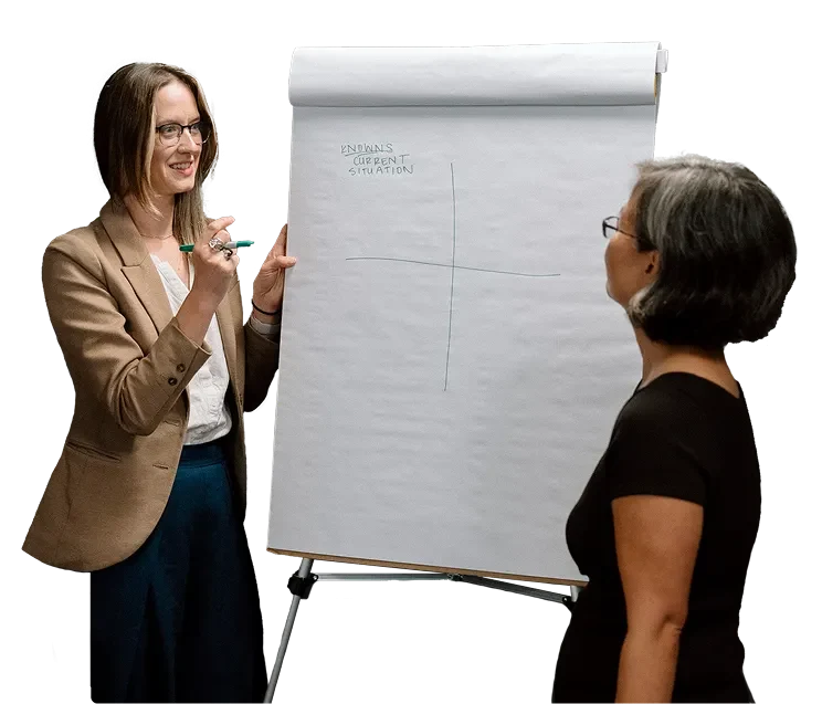 Photograph of Senior Analyst Emily Daman and Senior Advisor Katie Hong talking engaging in discussion in front of a flip chart. 