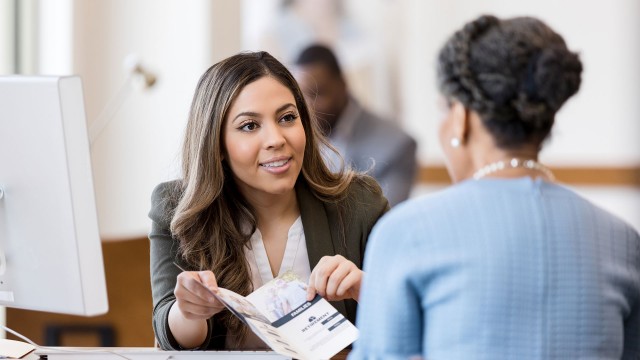 A banker shows a customer a brochure of services in credit union or bank setting. Both women are professionally dressed.