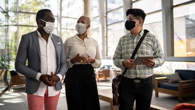 Three co-workers walking in an office lobby with their COVID-19 masks on