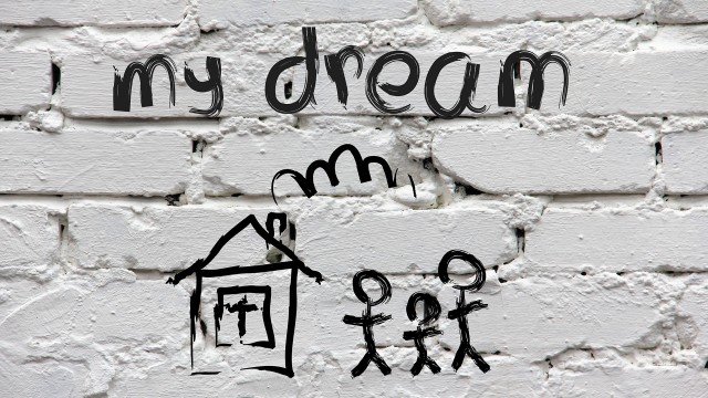 Kids sketch of house with stick figure family and the words "my dream" above it on background of painted white bricks