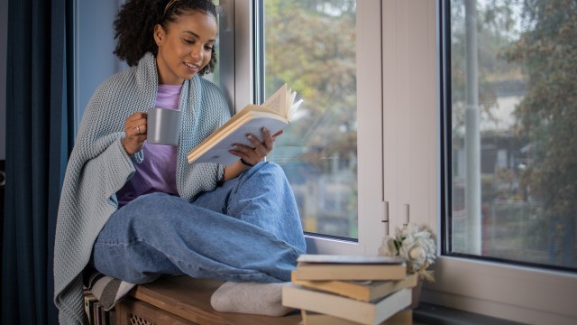 African American young woman reading a book at home at her cozy corner