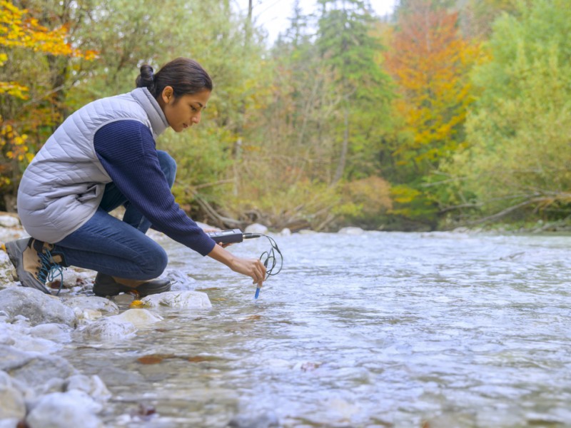Side view of young female biologist using multiparameter instrument while testing dissolved oxygen in river.
