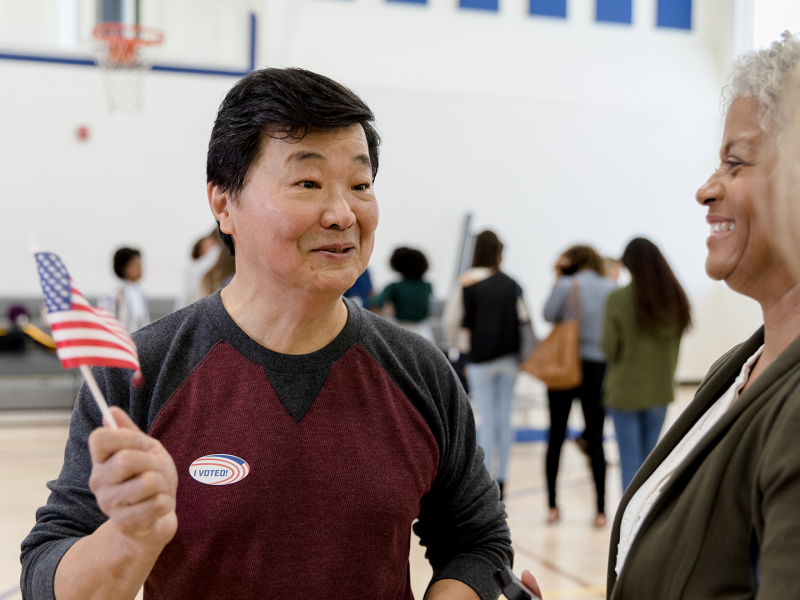 Man with an American flag talking to women at a voting center