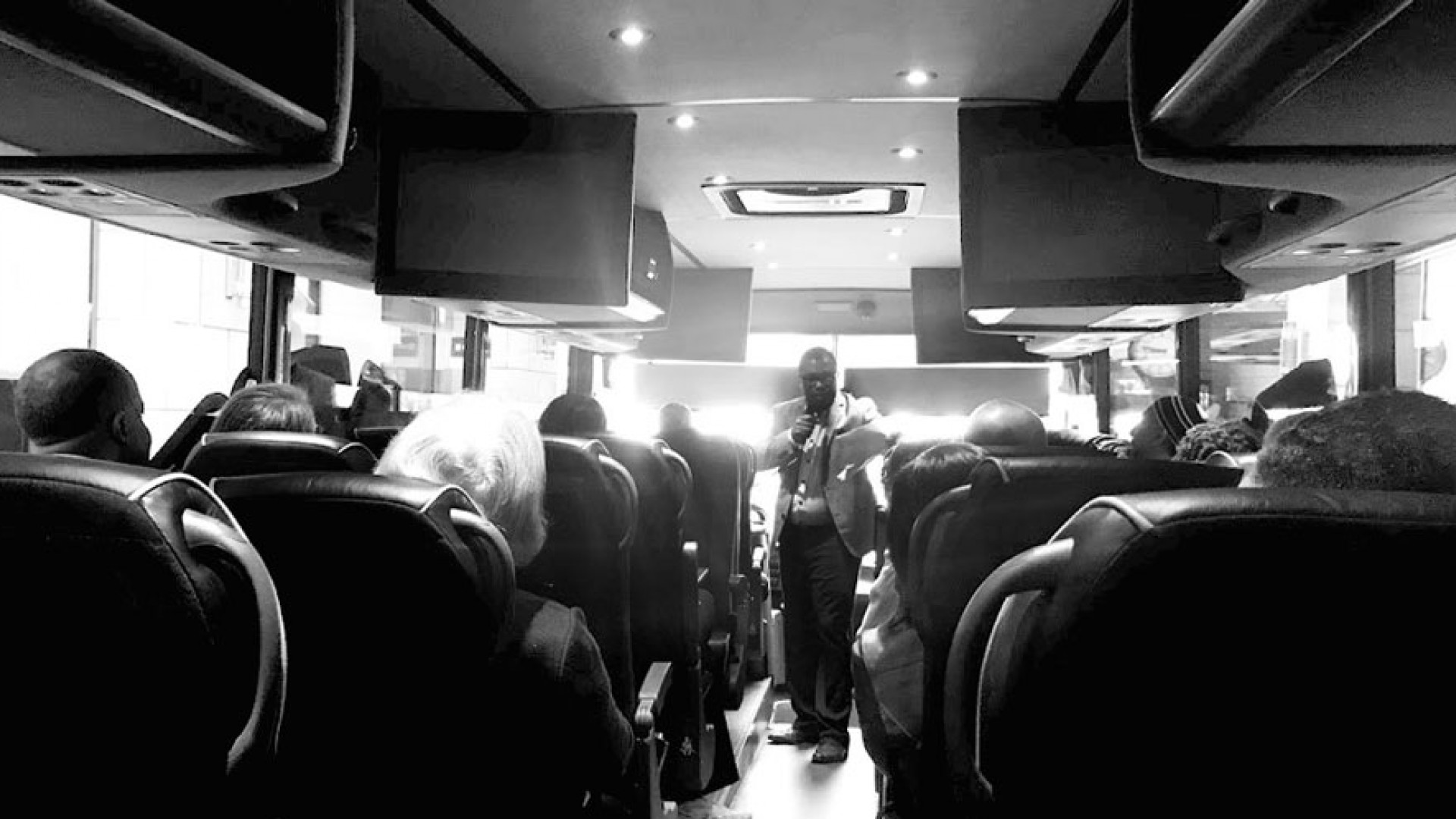 Black and white picture of Boukman Mangones speaking to people sittin on a bus