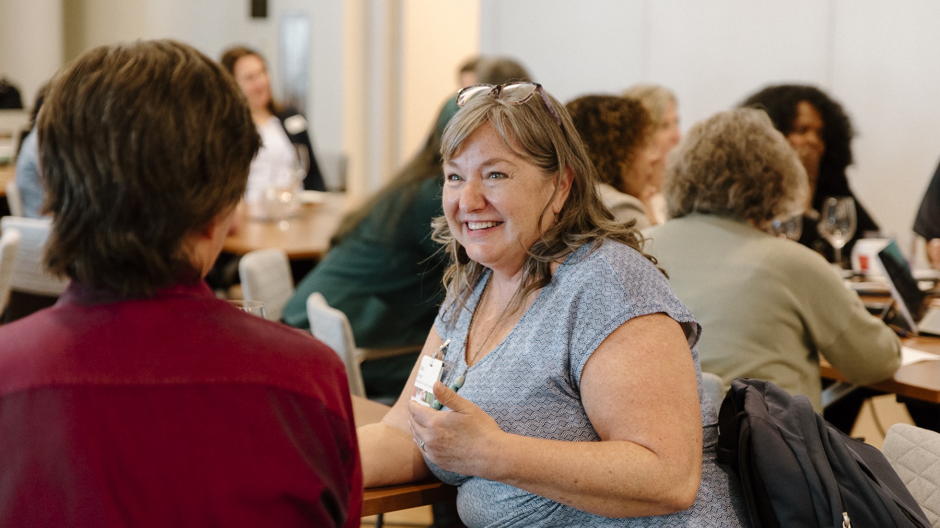 Photo from a BCP convening. There is a woman sitting in the center of the photo wearing a blue dress, talking to another attendee.