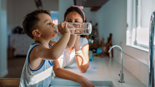 Boy drinking clean water by the sink with his mother.