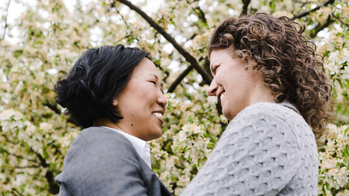 Interracial LGBTQ+ couple looking into each other's eyes in front of a blooming tree