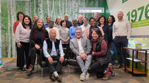Group photo of about 20 Philanthropy Northwest Board members, staff and partners at an office with a birch-tree wall mural. Several sit in front while others stand behind.