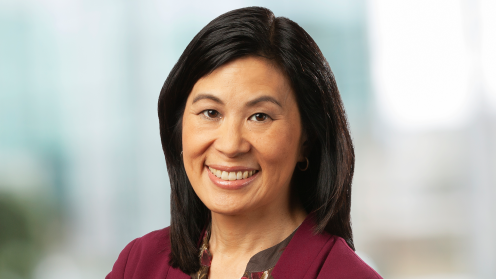 Headshot of Jill Nishi, smiling, with shoulder-length dark hair, wearing a burgundy blazer against a softly blurred indoor background.