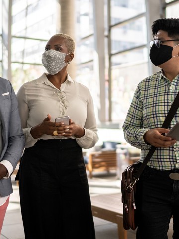 Three co-workers walking in an office lobby with their COVID-19 masks on