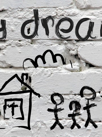 Kids sketch of house with stick figure family and the words "my dream" above it on background of painted white bricks