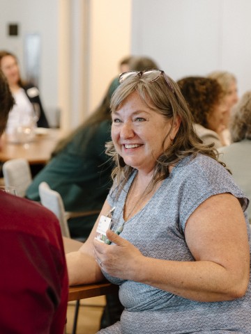 Photo from a BCP convening. There is a woman sitting in the center of the photo wearing a blue dress, talking to another attendee.