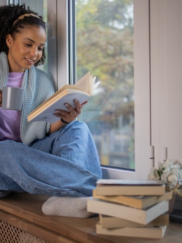 African American young woman reading a book at home at her cozy corner