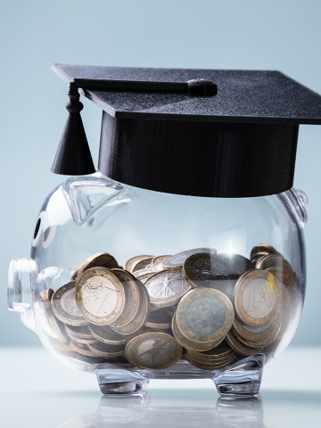Image of Black Graduation Hat on top of a clear piggybank with coins visible inside 