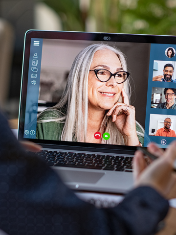 Image of a person looking at a laptop with 5 people on video conference 