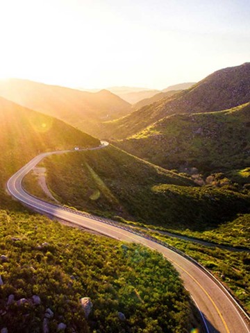Picture of sunshine breaking over hills into a rural valley with a two lane winding road