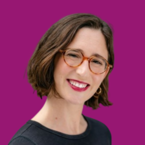Headshot of Aviva Stampfer, smiling with short brown hair and wearing round glasses, hoop earrings and a dark top, against a ube colored background.