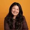 Headshot of Samona Norombaba smiling infront of an orange background.