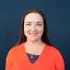 Headshot of Megan Sukys smiling and wearing an orange shirt over a dark blue background