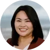 Headshot of Meredith Higashi, smiling, with shoulder-length black hair, wearing a burgundy blazer over a white top against a softly blurred outdoor background.