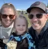 Photo of Alessandra Frichtl smiling outdoors with two family members, all wearing sunglasses, with snowcapped mountains and a bright blue sky in the background.